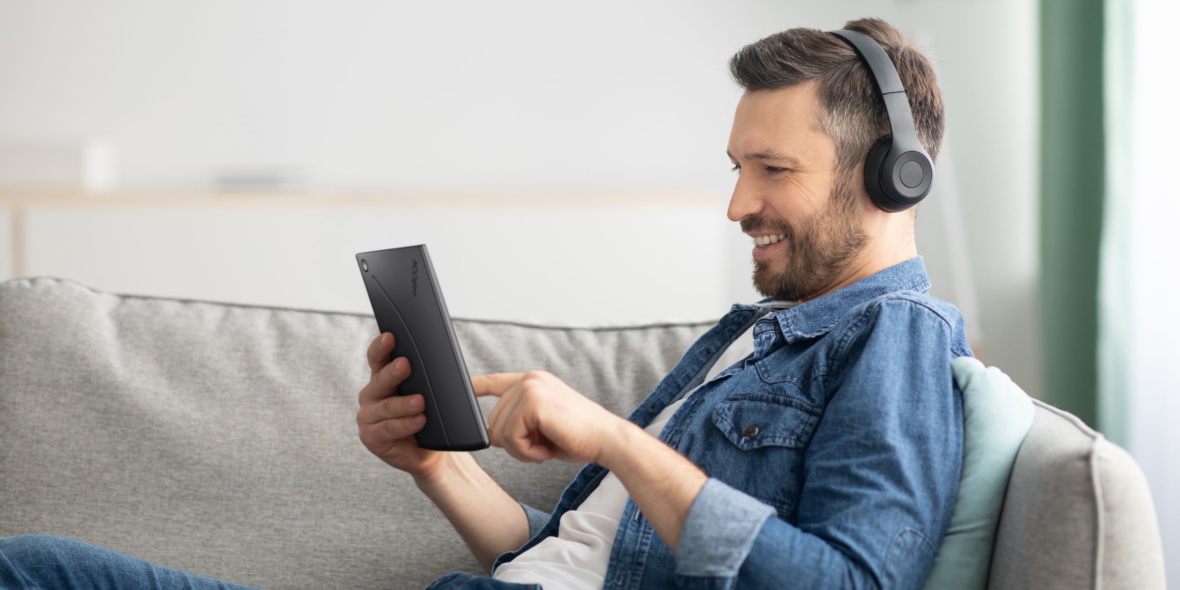 man reading and listening on inkBOOK Solaris e-book reader sitting n the sofa
